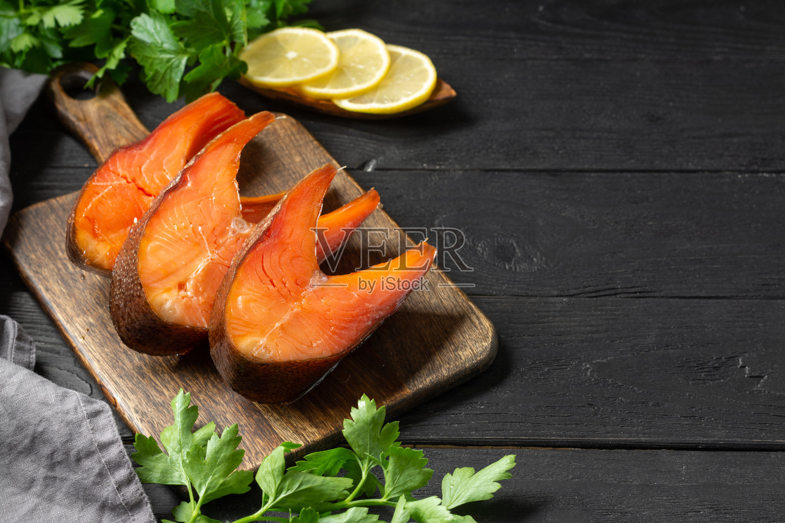 熏鱼鳟鱼。餐板上的熏鱼排。切成片的烟熏鳟鱼躺在厨房的木桌子上。熏鳟鱼特写照片摄影图片