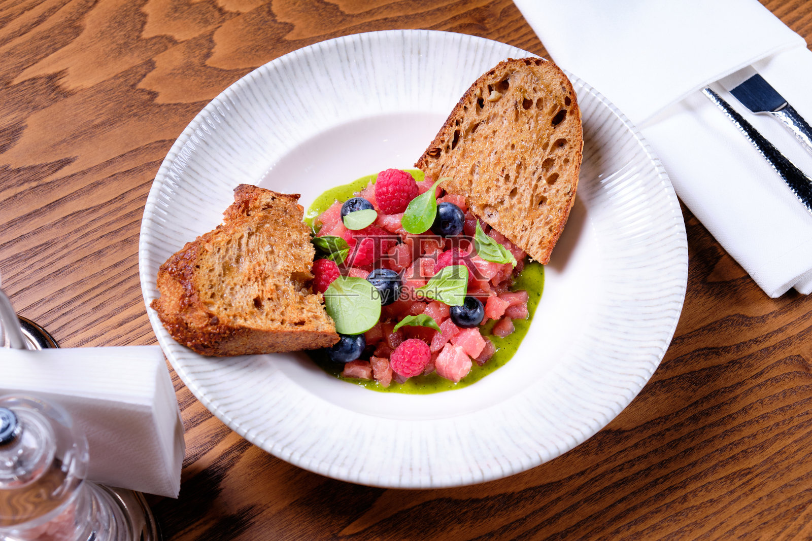 金枪鱼鞑靼与覆盆子和蓝莓在一个白色的盘子。照片摄影图片