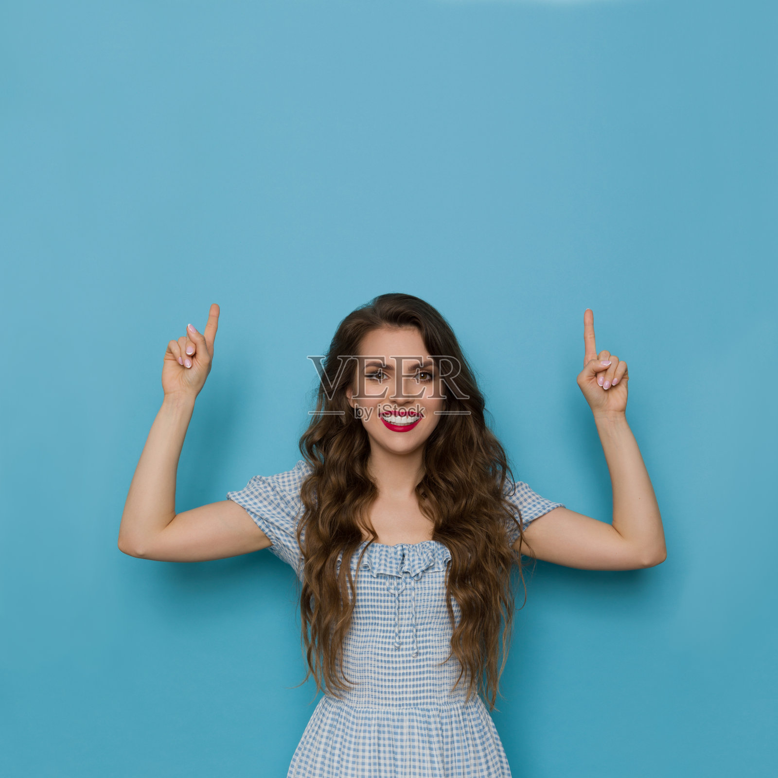 穿着蓝色连衣裙的美丽年轻女子正在向上指照片摄影图片