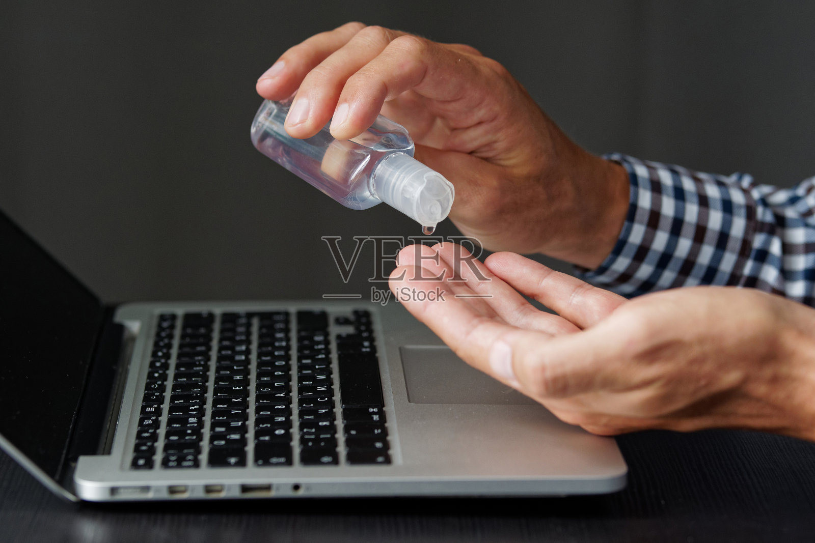 特写镜头。洗手液抗菌在手，笔记本电脑，笔记本电脑，手机。视图上的深色木桌子和人的背景。阻止covid-19、冠状病毒的传播。照片摄影图片