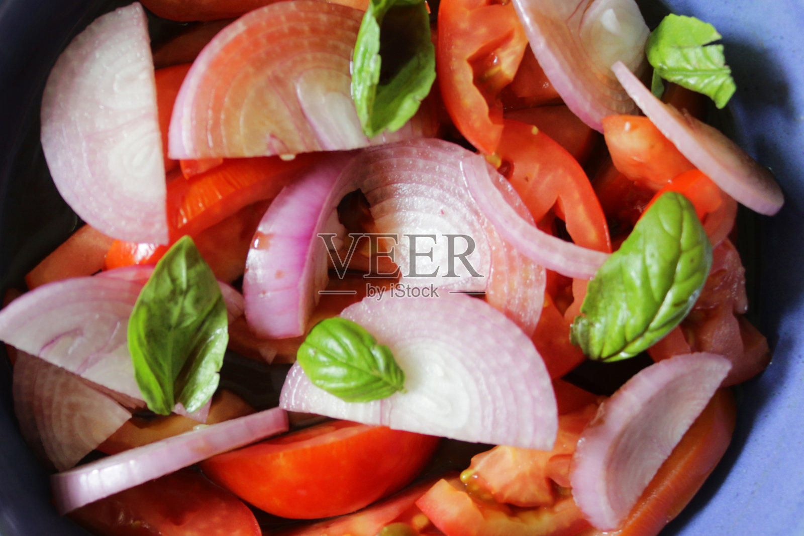 这是自制番茄洋葱沙拉的特写图片，配以罗勒叶，放在一个蓝色的碗里照片摄影图片
