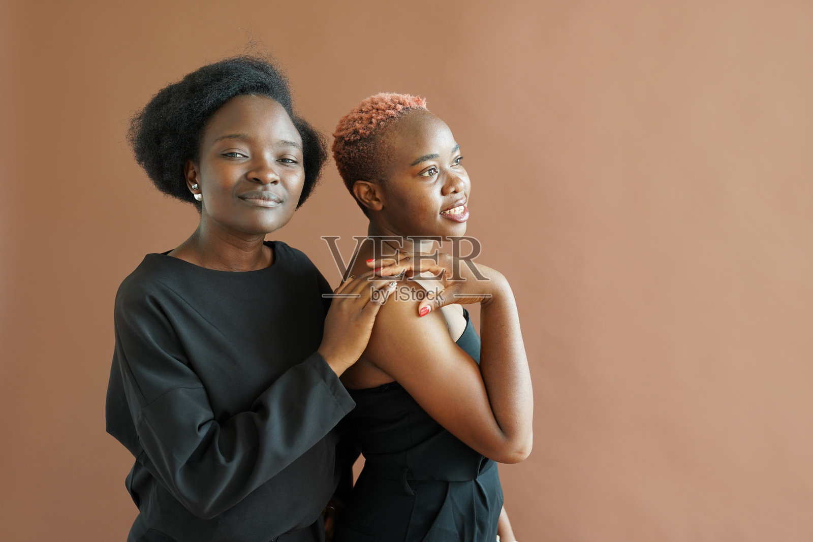 两个友好的非洲裔美国女孩在棕色背景的演播室里轻轻地拥抱。抗议照片摄影图片