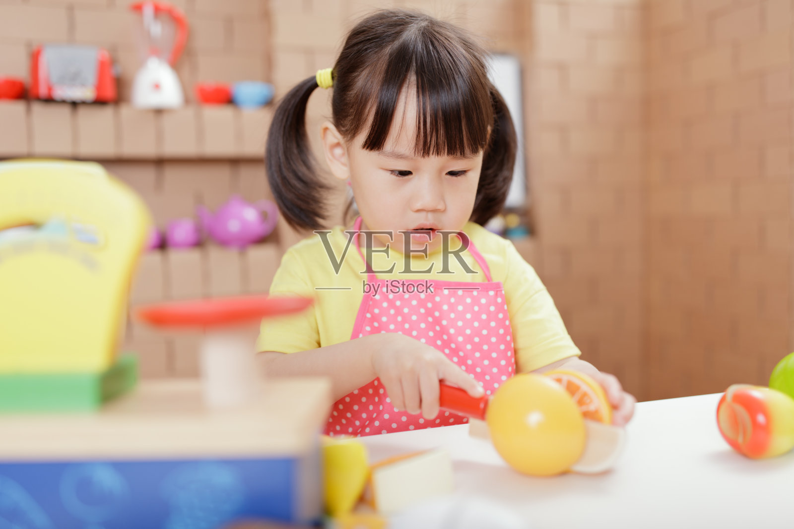 蹒跚学步的小女孩以纸板店为背景，假装扮演准备食物的角色照片摄影图片