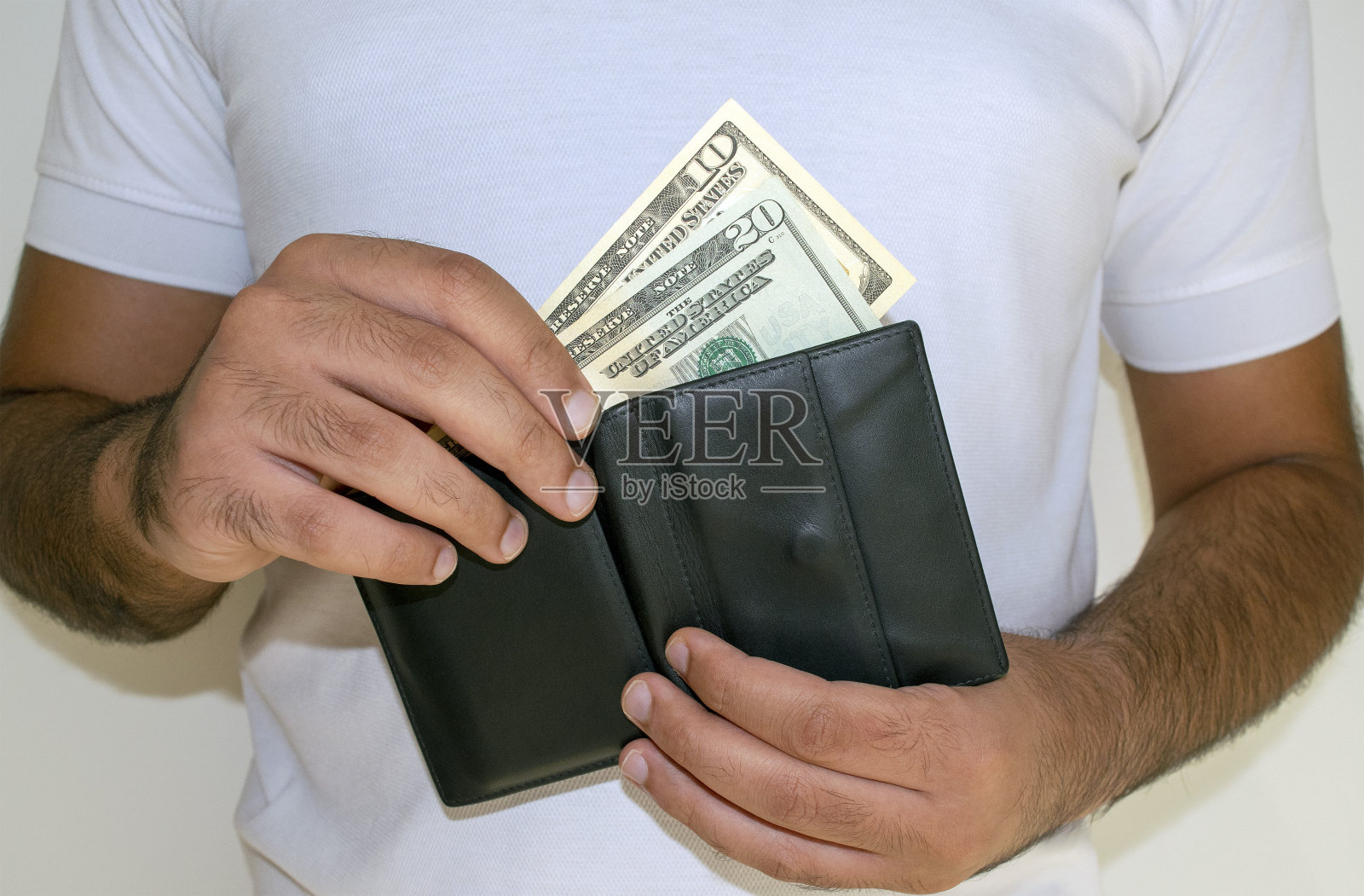 穿白色t恤的男子把美元钞票放进了黑色的钱包照片摄影图片