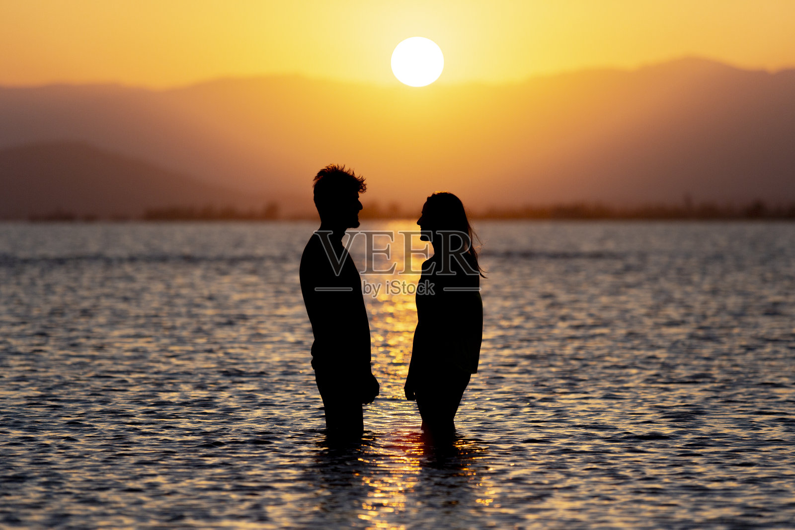 日落时分，一对年轻的夫妇站在海滩的水里照片摄影图片