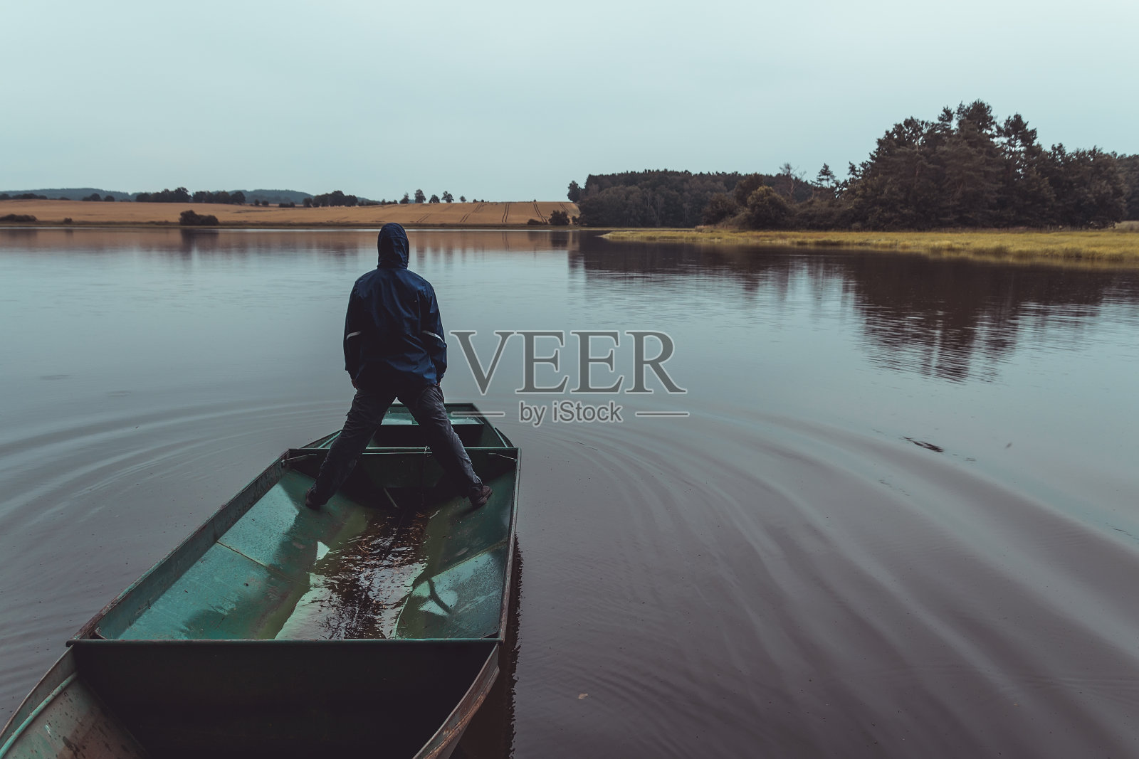 一个人站在池塘里的渔船上，伴着青草、树木和田野的喜怒无常的天气。捷克共和国，调色照片照片摄影图片