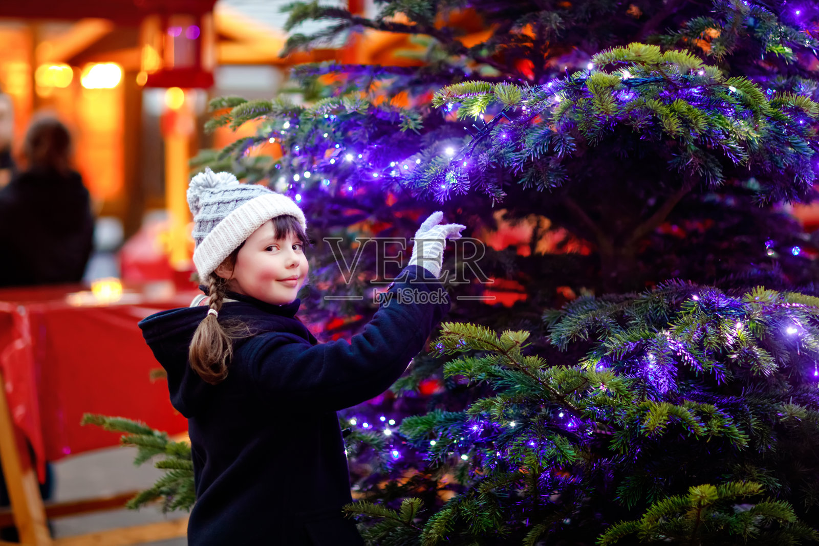 可爱的小女孩在传统的圣诞市场在大雪期间玩。快乐的孩子享受德国传统家庭市场。女生站在发光的圣诞树旁。照片摄影图片
