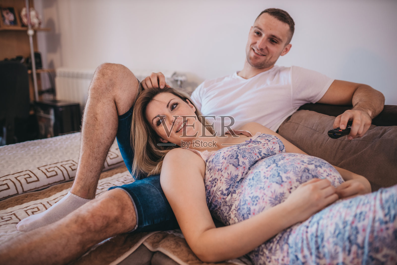 年轻的丈夫和他怀孕的妻子坐在家里的沙发上看电视照片摄影图片