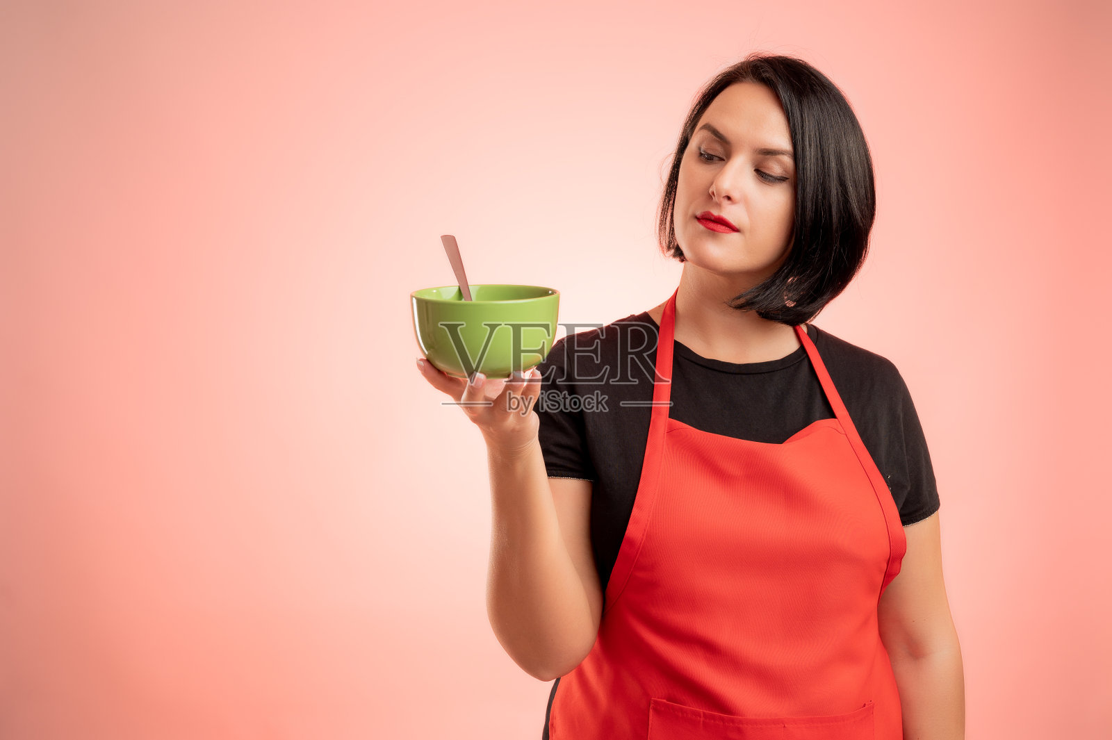 一名在超市工作的妇女，穿着红围裙和黑t恤，手里拿着碗照片摄影图片