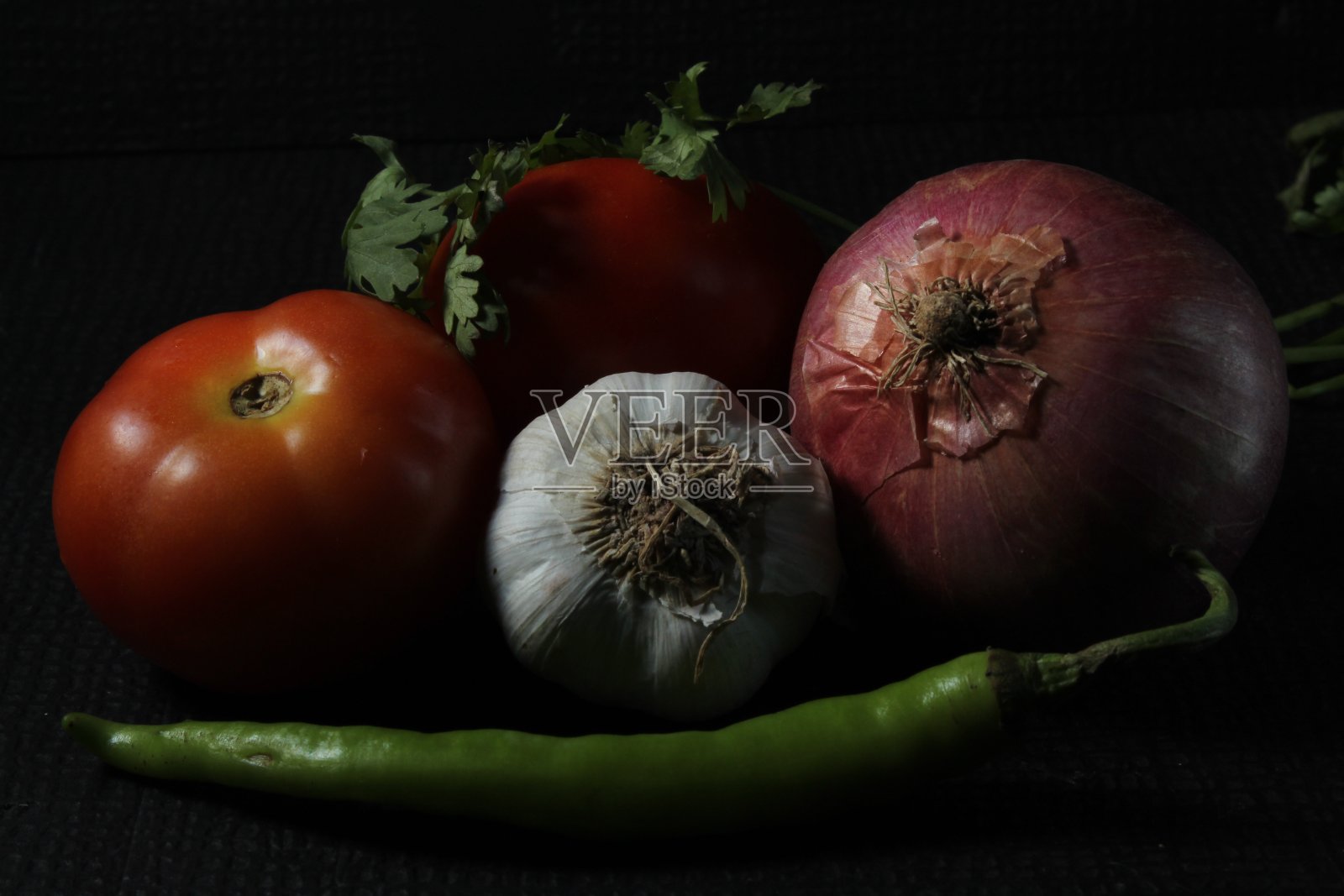 绿色的辣椒，大蒜，番茄，洋葱和咖喱叶被孤立在黑色的背景。组成的概念。辛辣的青椒，新鲜成熟的番茄，黑色背景的洋葱。照片摄影图片