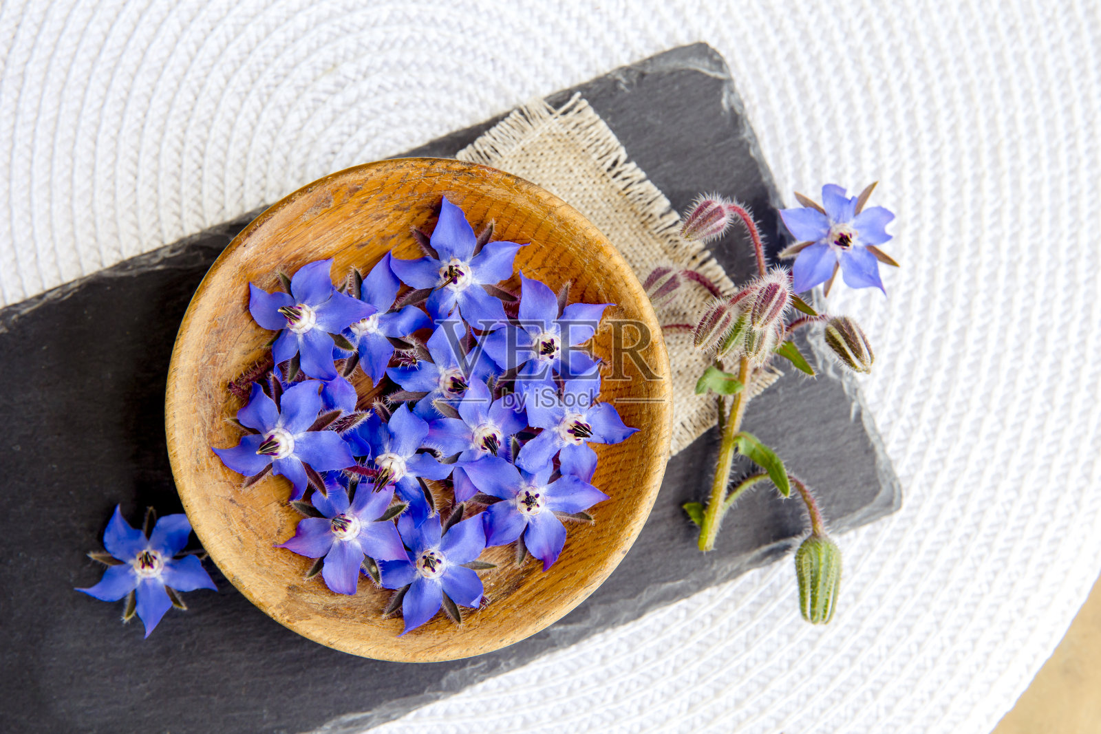 用美丽的深蓝色食用花作食物装饰Borago officinalis (Borago或borage)。白色背景，黑色石盘，木碗中花朵的平置视图。照片摄影图片