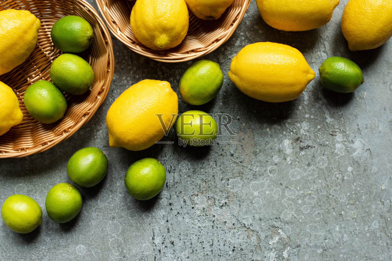 俯视图成熟的黄色柠檬和绿色的酸橙在柳条篮子在混凝土纹理表面照片摄影图片