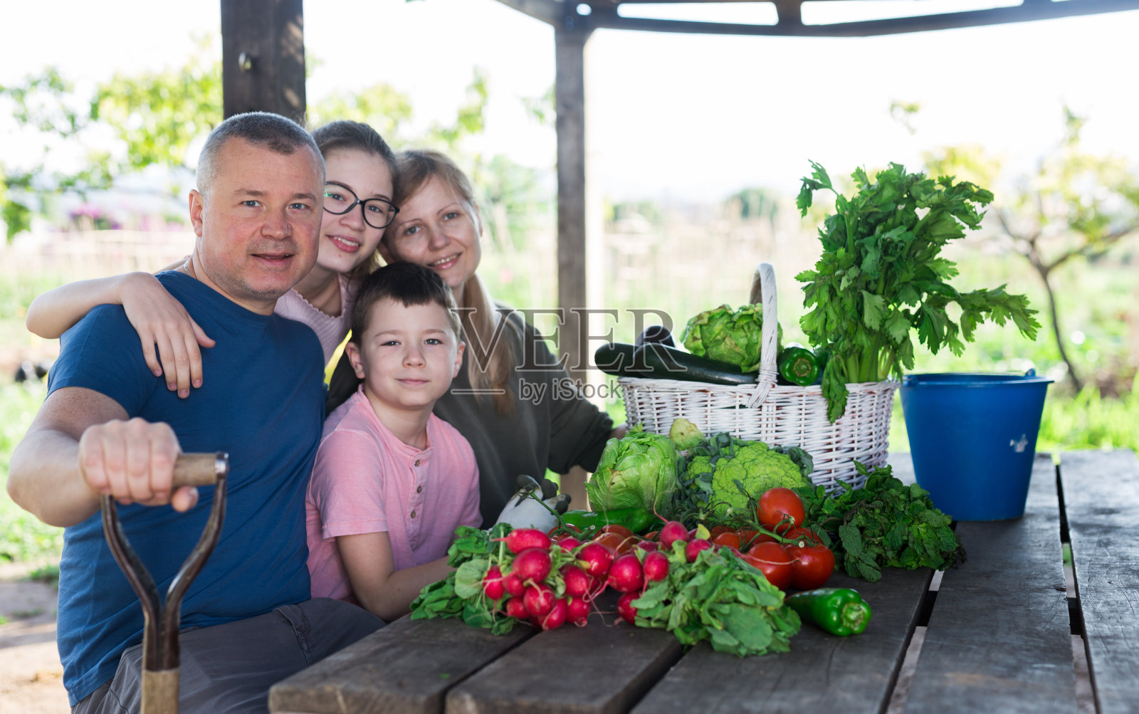 一家人微笑着坐在户外，吃着收获的蔬菜照片摄影图片