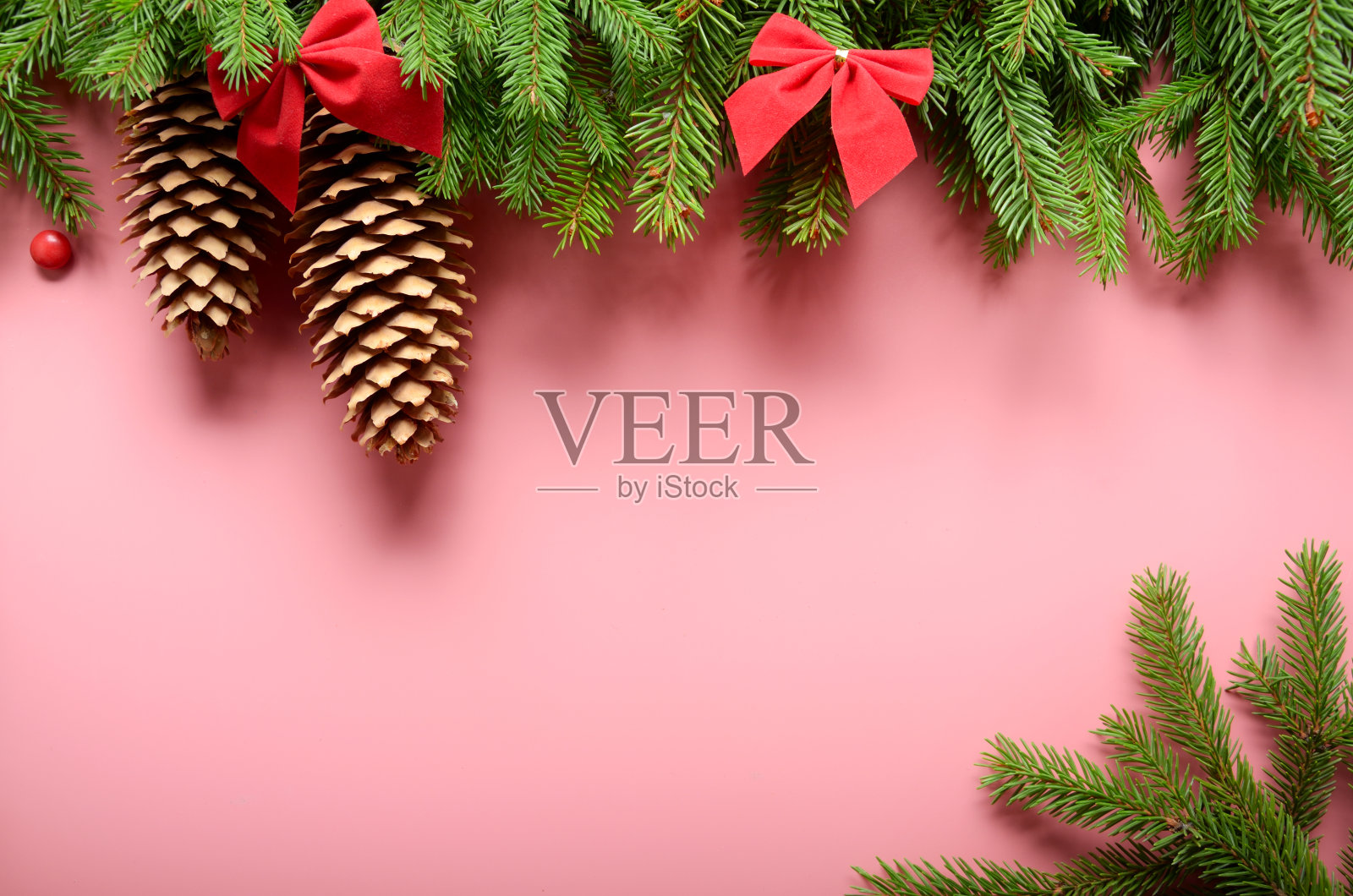 平铺设计的圣诞贺卡的冷杉树枝，蝴蝶结和锥形在粉红色的背景。空间的文本照片摄影图片