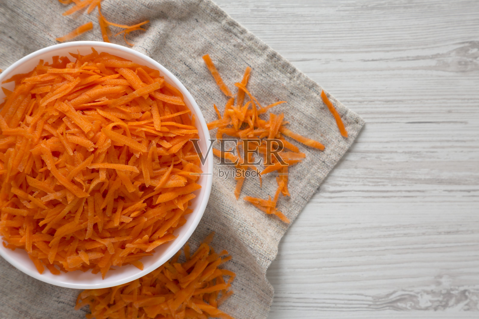 白木背景下的白碗里放着切碎的胡萝卜，俯视图。平躺，头顶，头顶。照片摄影图片