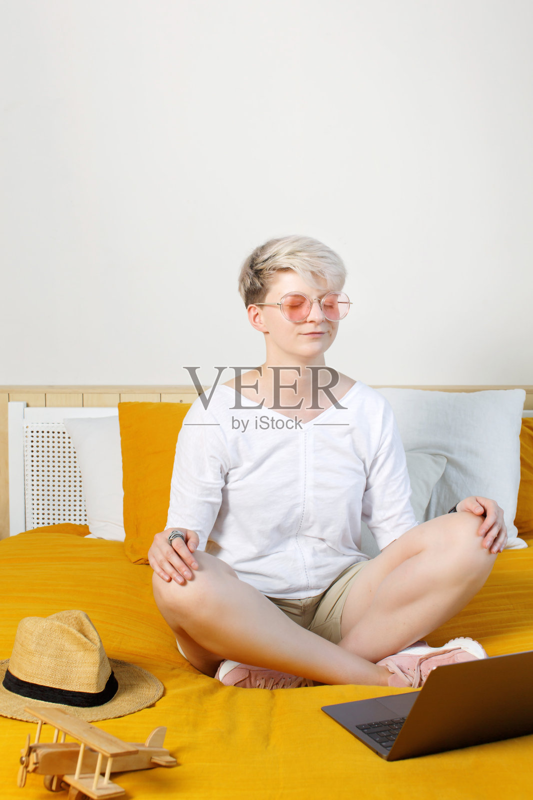 黎明时分，金发漂亮的时髦年轻女子坐在床上，坐在笔记本电脑前，在网上冥想，照片摄影图片