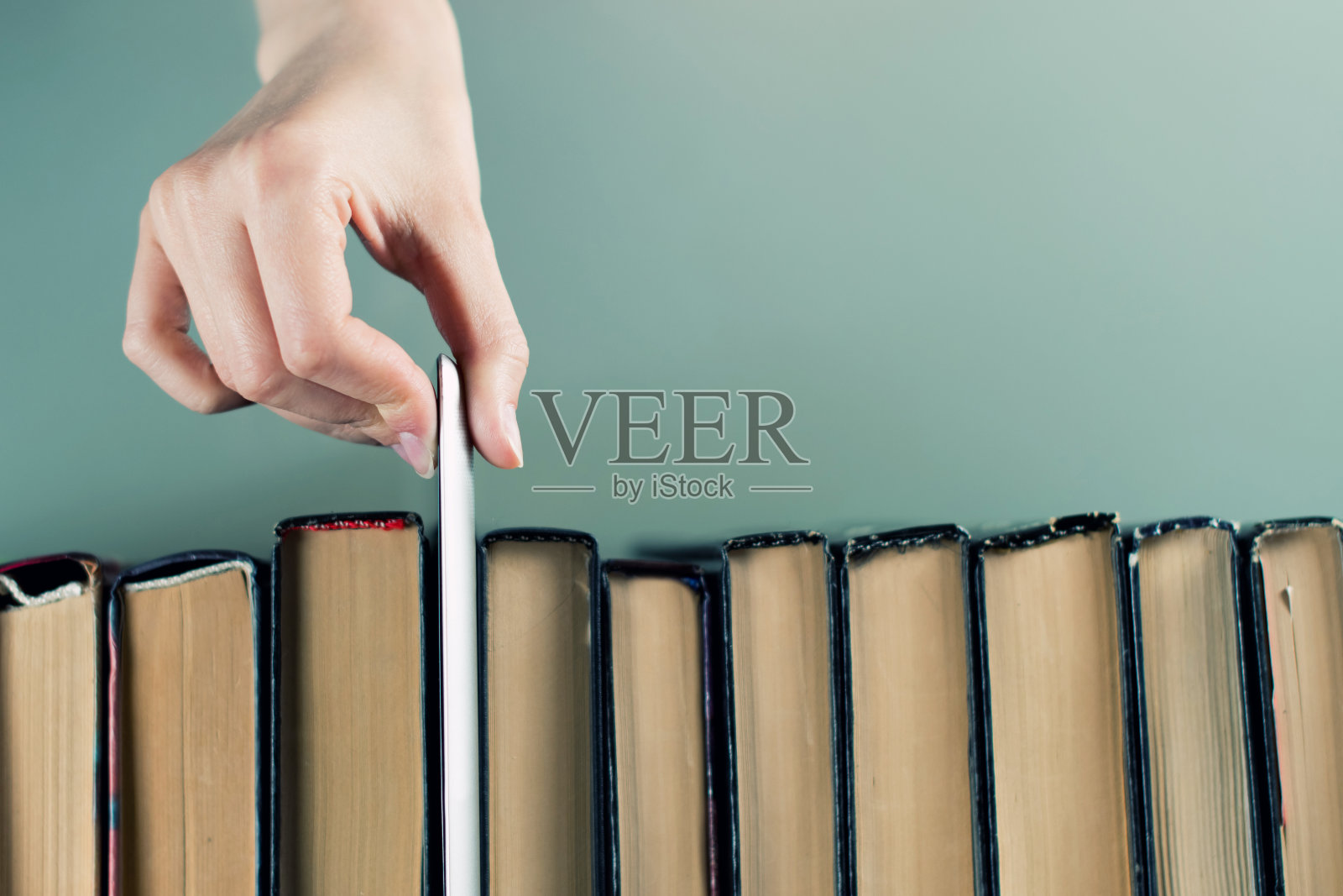 手从一排旧纸质书中拿出一个重新设计的平板电脑，俯视图照片摄影图片