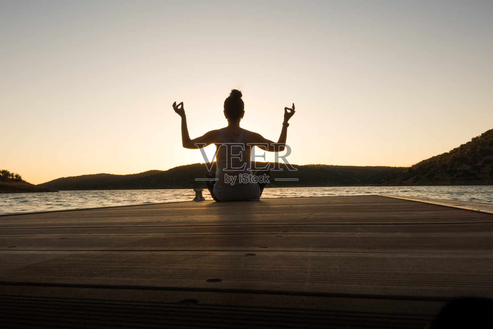 日落时分，小女孩在码头上做瑜伽。完美的姿势照片摄影图片