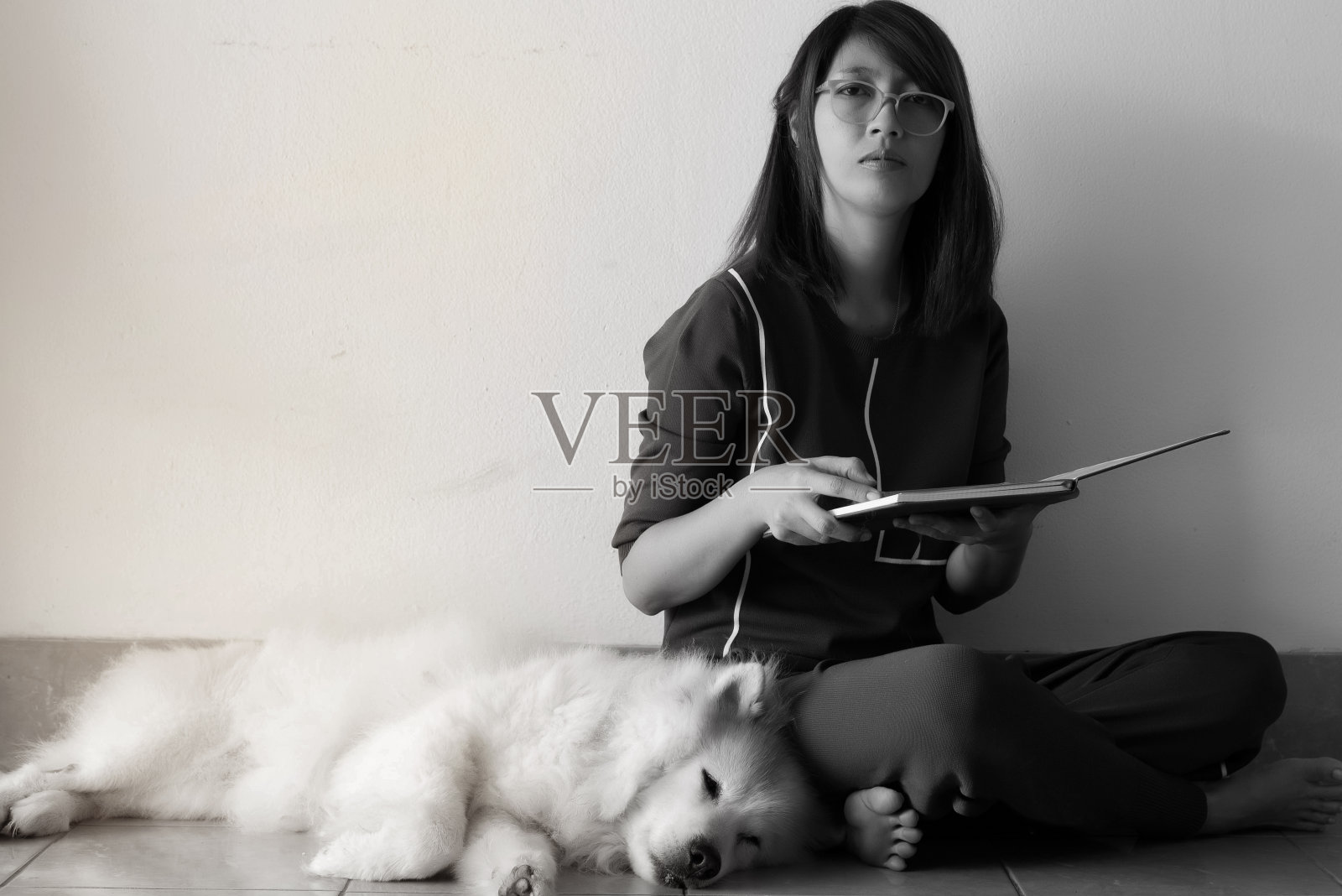 女士坐在她的狗旁边看书，黑白色调，周围模糊的光线照片摄影图片