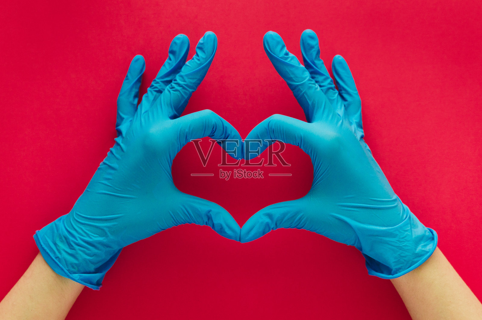 一个女人的手与手套形成一个心，她的手指在红色的背景照片摄影图片