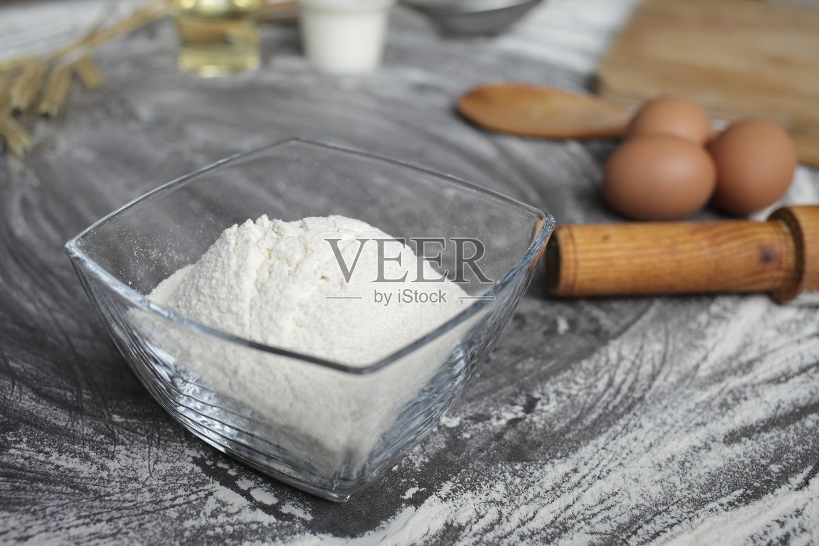 面粉，鸡蛋，橄榄油，牛奶，麦穗，厨房工具在灰色的背景。照片摄影图片