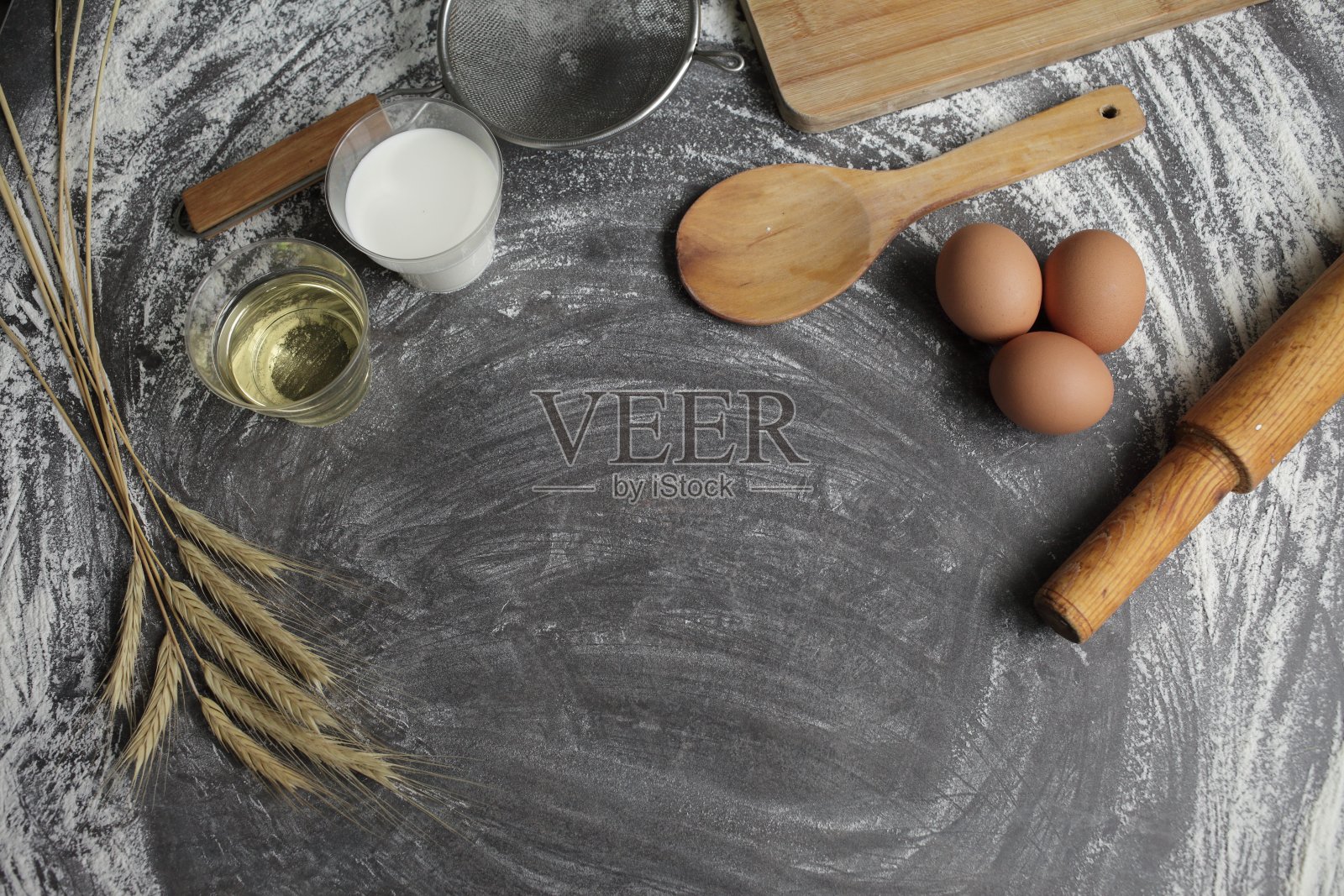 鸡蛋，面粉，橄榄油，牛奶，麦穗，厨房工具的灰色背景。照片摄影图片