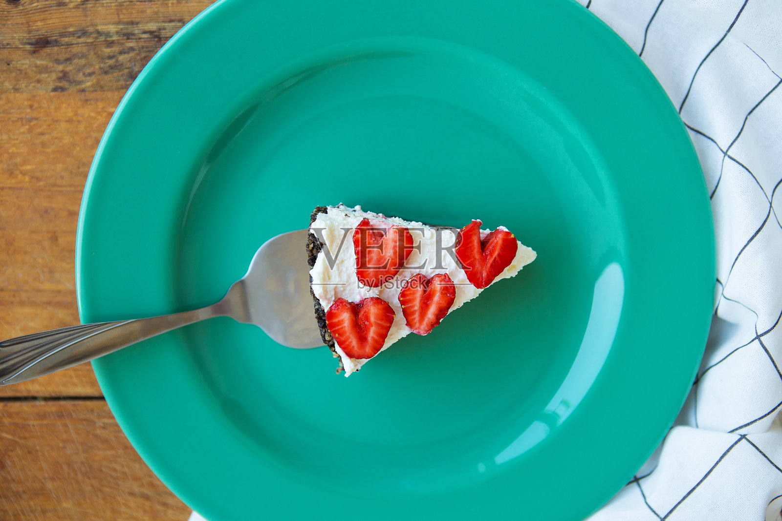 一块装饰着心形草莓的草莓芝士蛋糕放在薄荷色的盘子上，放在格子餐巾上。从以上观点。照片摄影图片