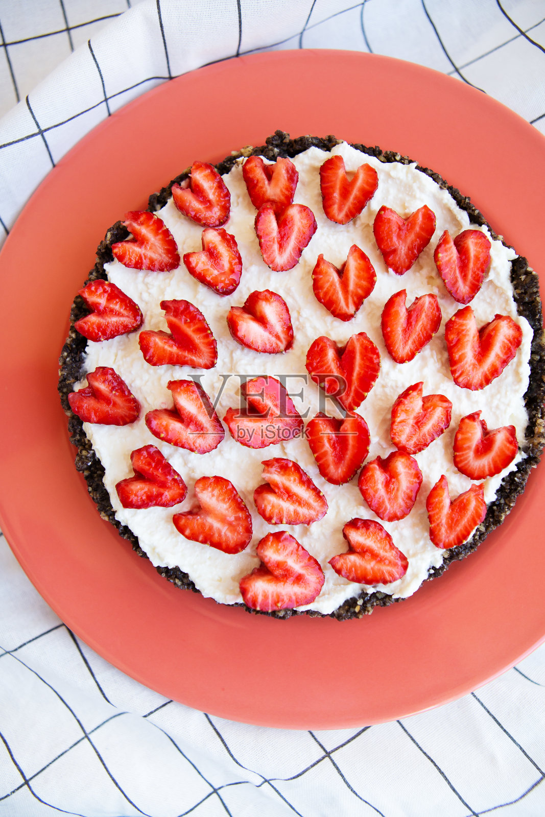 装饰着心形草莓的草莓芝士蛋糕放在一个珊瑚色的盘子上，放在一张餐巾纸和一张木桌上。图示:草莓芝士蛋糕食谱。照片摄影图片