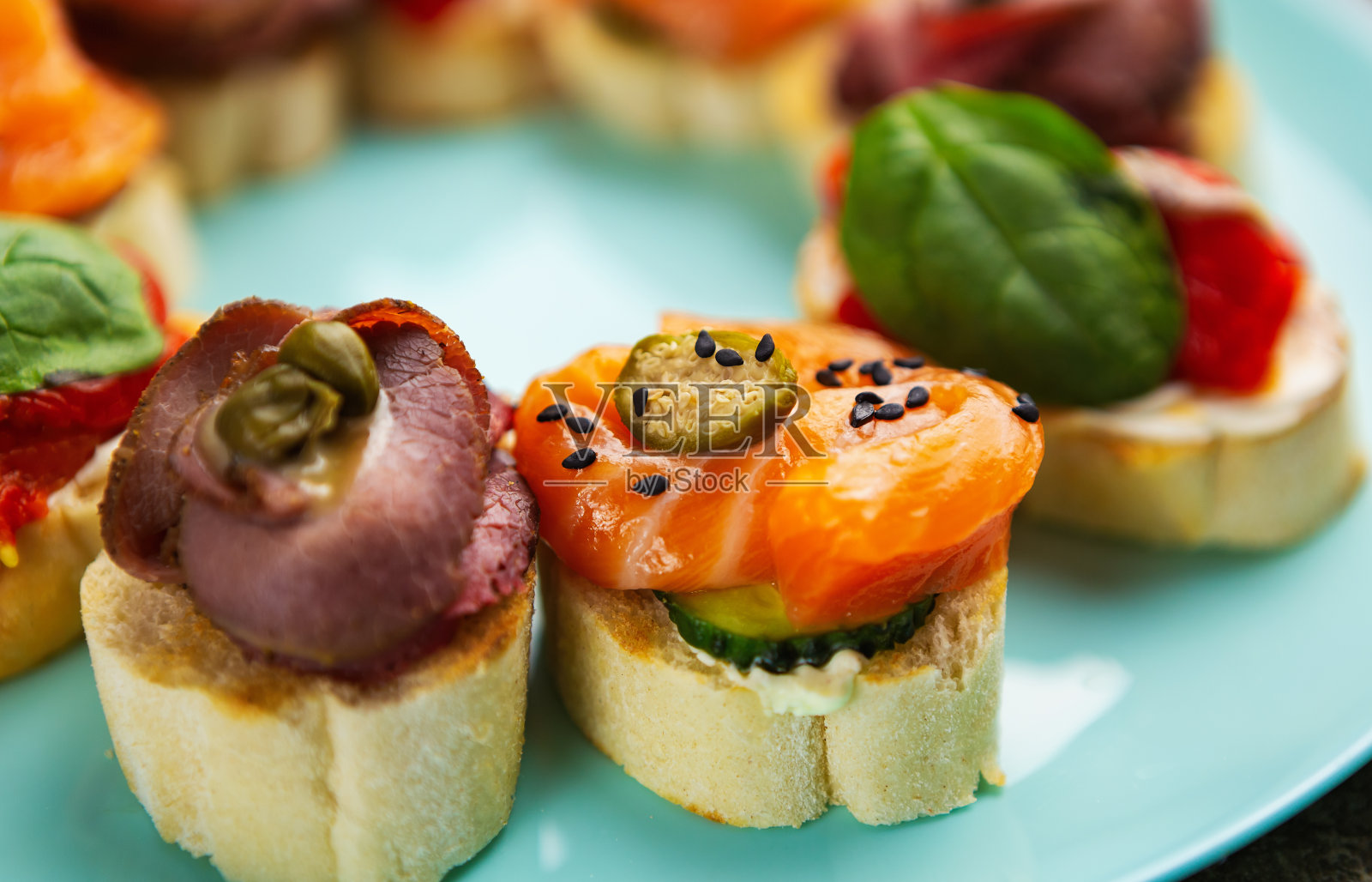 餐前小吃:三文鱼片、小牛肉、面包上的酸豆，放在蓝色盘子里。照片摄影图片