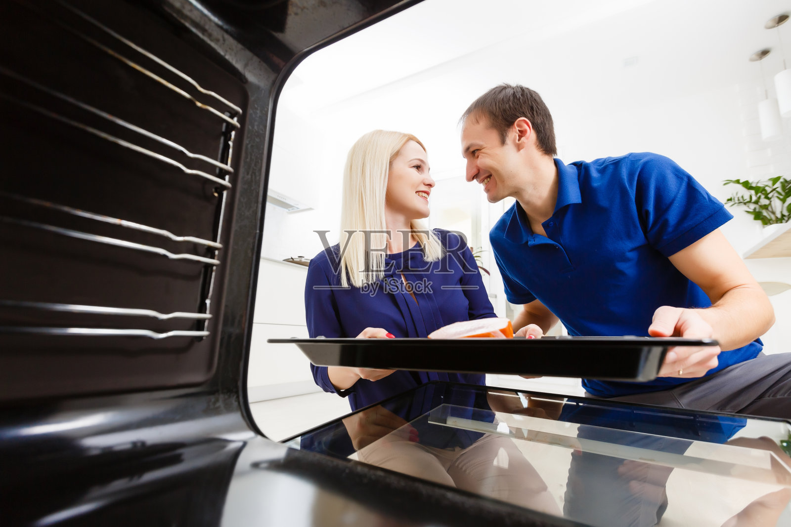 一对年轻夫妇在厨房准备食物的肖像。年轻的家庭主妇手里拿着刚烤好的肉照片摄影图片