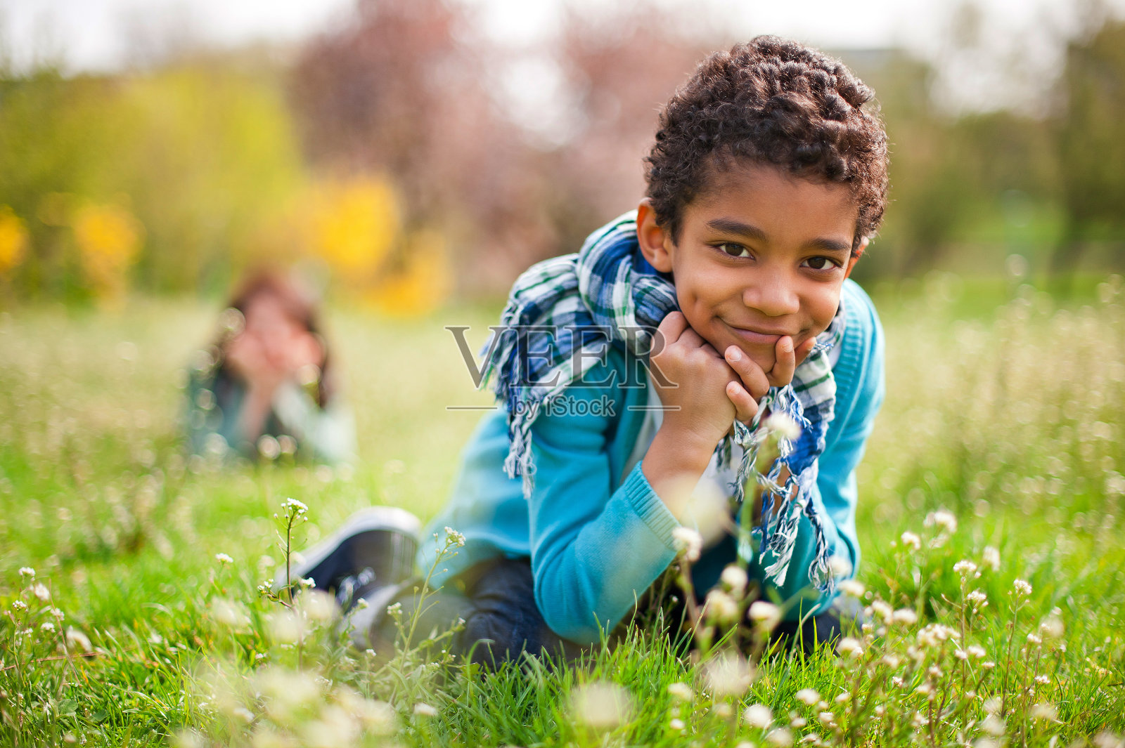 可爱的小黑孩坐在花地里笑着。照片摄影图片
