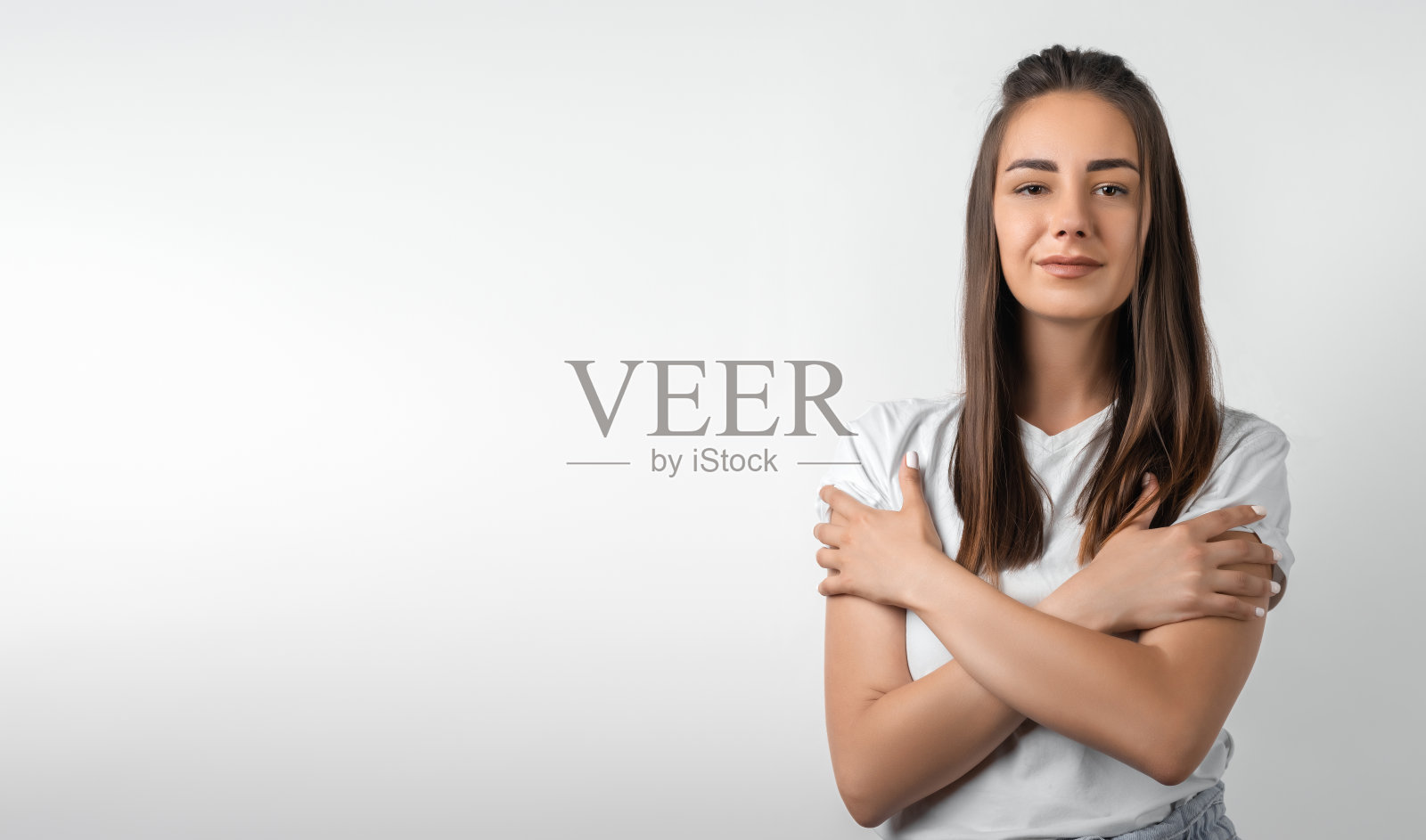 爱、关怀、温柔的概念。迷人的欧洲年轻女子栗色长发站立，交叉双臂在胸前，在白色的背景照片摄影图片