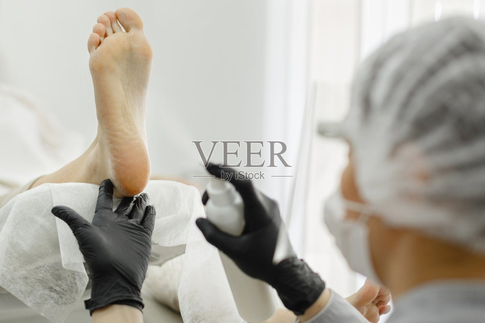 专业修脚的过程。一个戴着防护面具的师傅给女性的腿按摩。照片摄影图片