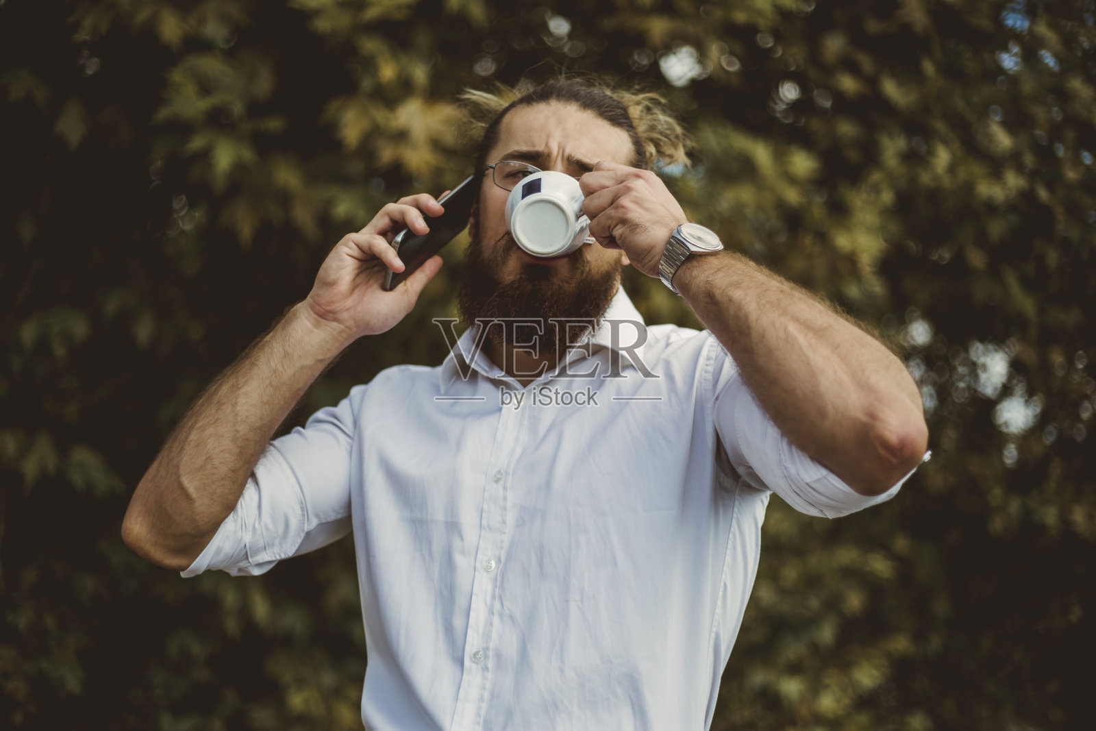 一个年轻的商人有一个咖啡休息的肖像-年轻的商人长头发-咖啡休息在办公大楼的露台上照片摄影图片