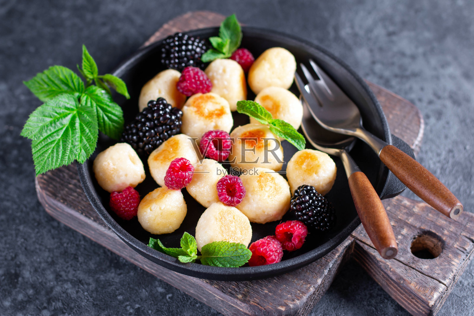 慵懒的乡村奶酪饺子配上覆盆子、黑莓和薄荷，背景是深色的混凝土。照片摄影图片