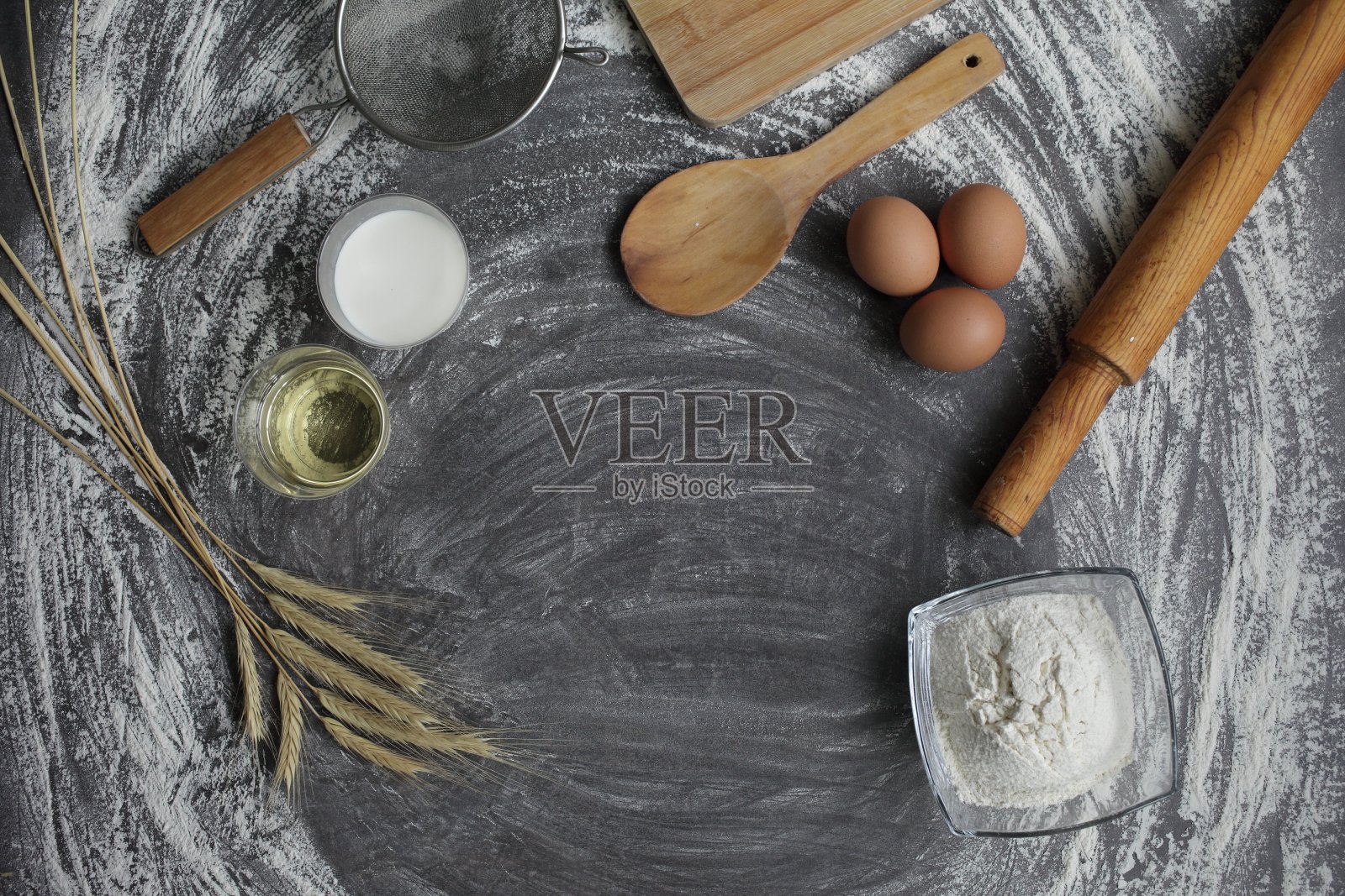 鸡蛋，面粉，橄榄油，牛奶，麦穗，厨房工具的灰色背景。照片摄影图片