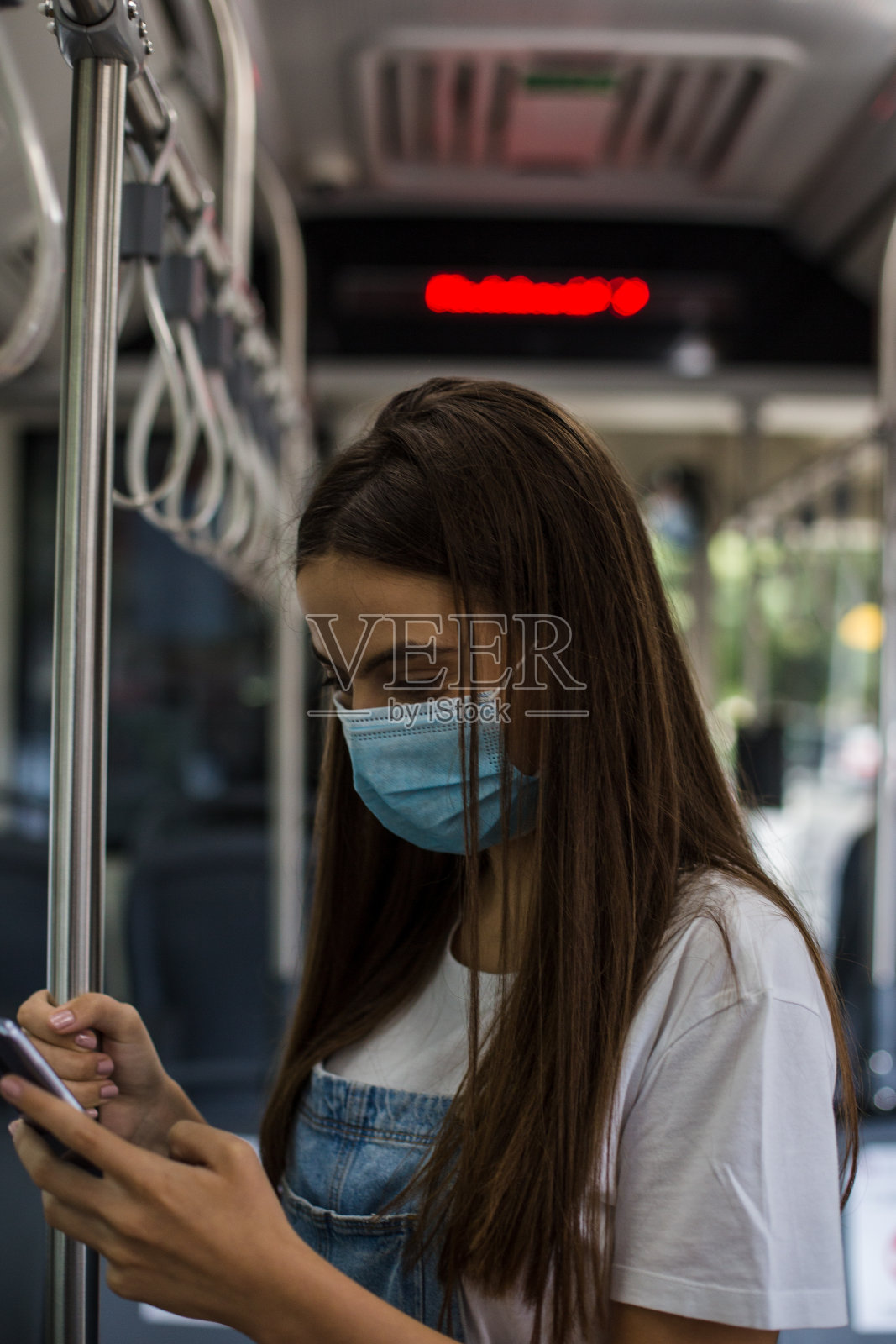 年轻女子戴着口罩在公交车上用智能手机照片摄影图片