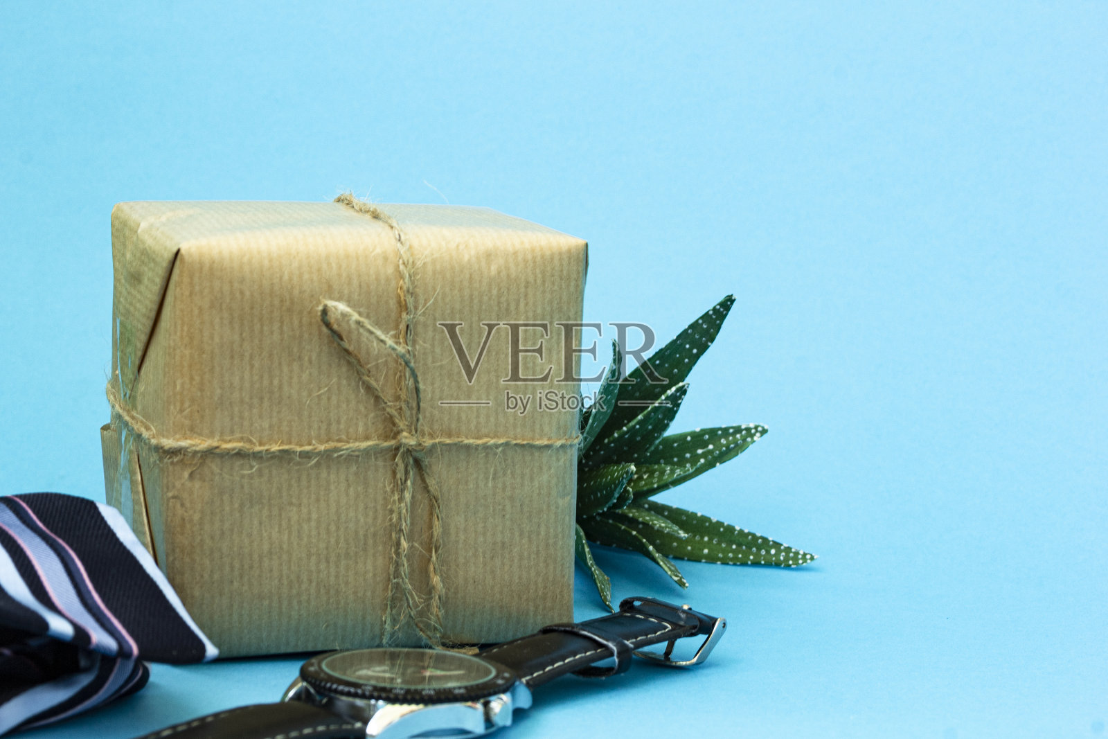 工艺礼品与黄麻绑在一个蓝色的背景。旁边放着一条蓝色条纹领带、一块男士手表和一朵绿色多肉花。副本的空间。男人祝贺的概念。照片摄影图片