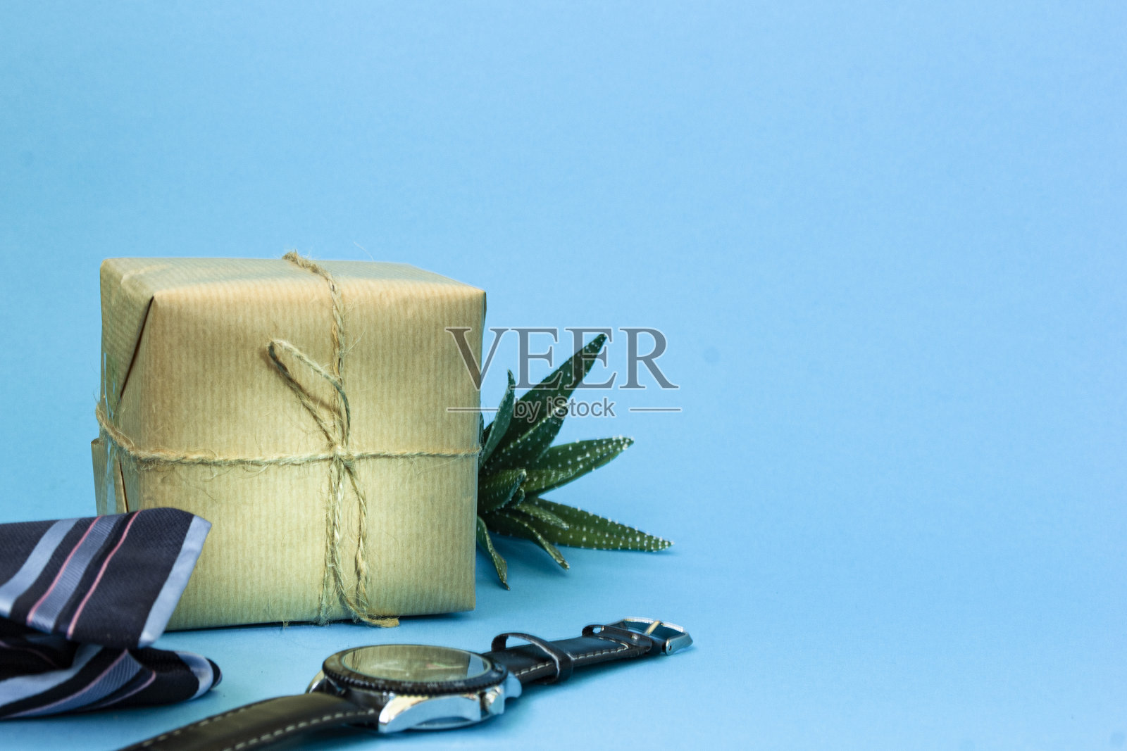 工艺礼品与黄麻绑在一个蓝色的背景。旁边放着一条蓝色条纹领带、一块男士手表和一朵绿色多肉花。副本的空间。男人祝贺的概念。照片摄影图片