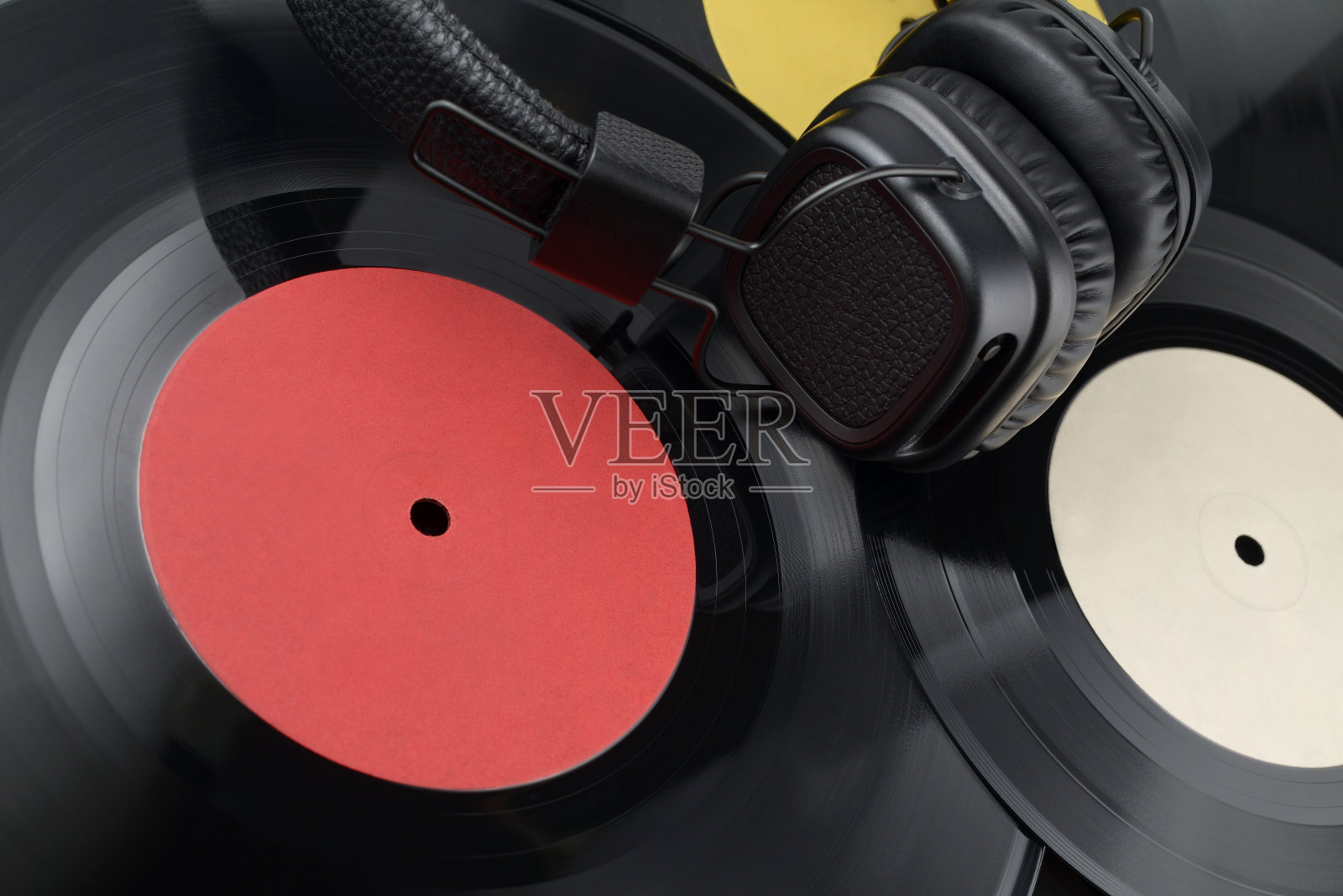 耳机放在一堆不同的黑胶唱片上。照片摄影图片