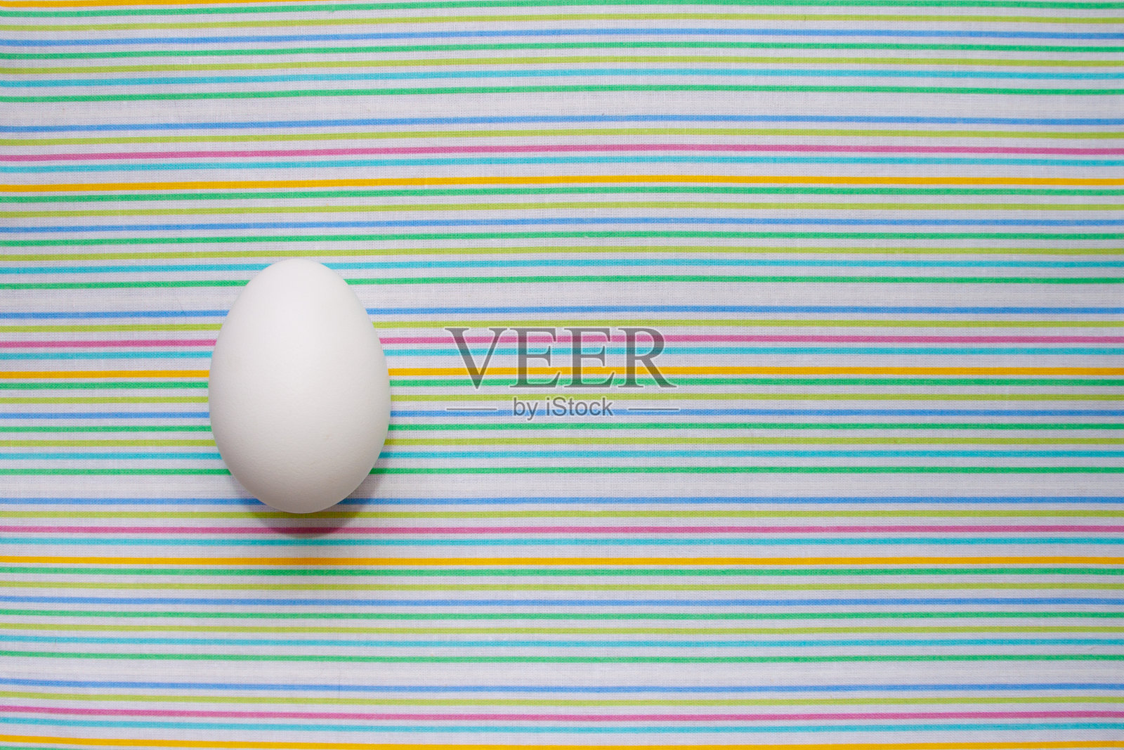白色的鸡蛋放在明亮的条纹桌布上。专为家禽业设计，生产生态生物天然食品。文本的空闲空间。简约的高级视图。设计横幅，卡片。照片摄影图片