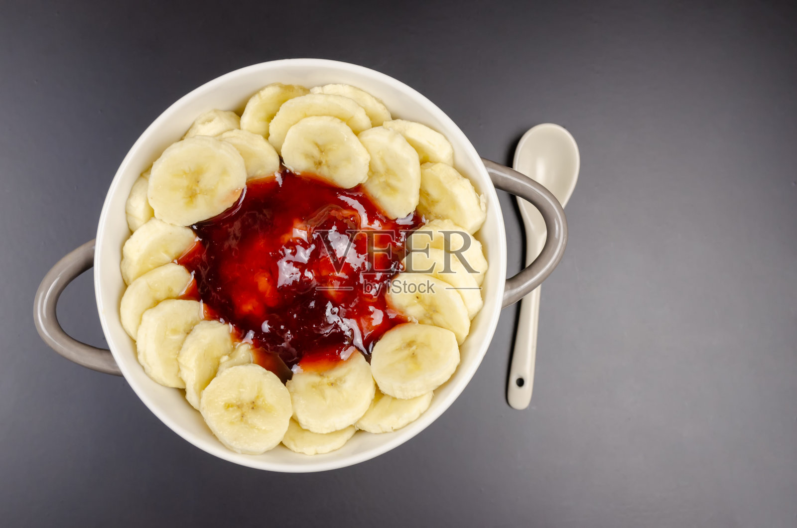 燕麦和香蕉，果酱在灰白色的碗和白色的勺子在黑色的背景，俯视图，复制空间。健康的早餐。照片摄影图片