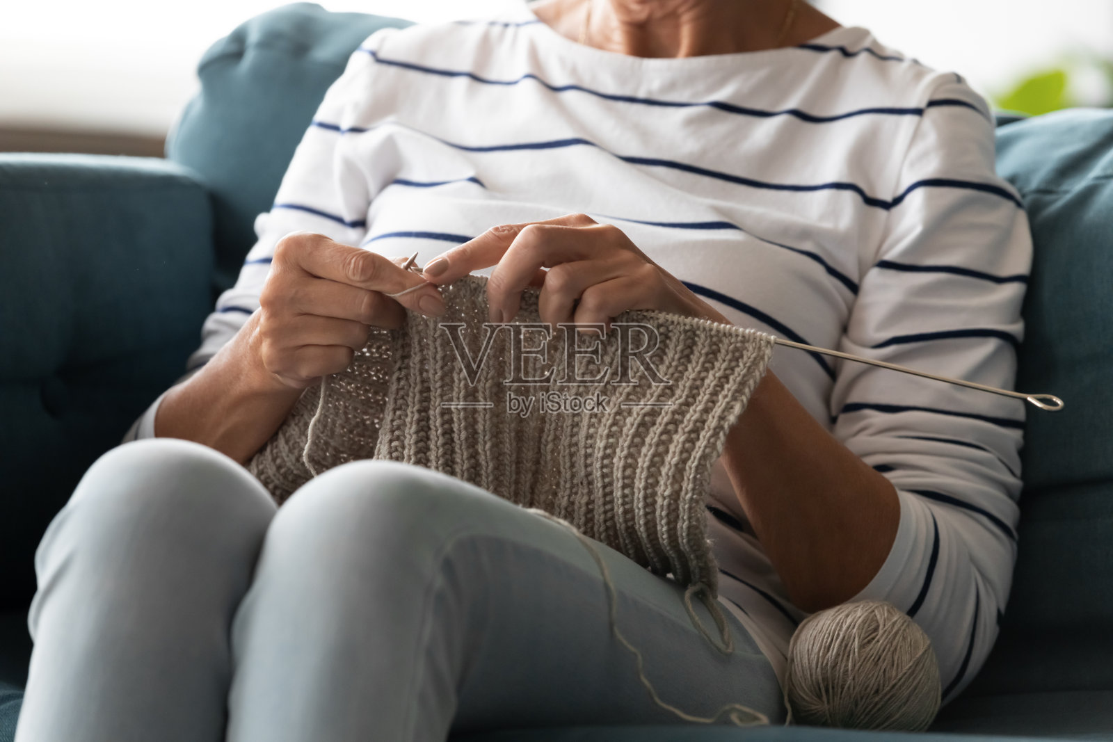 近旁的老妇人在织毛线，坐在家里的沙发上照片摄影图片