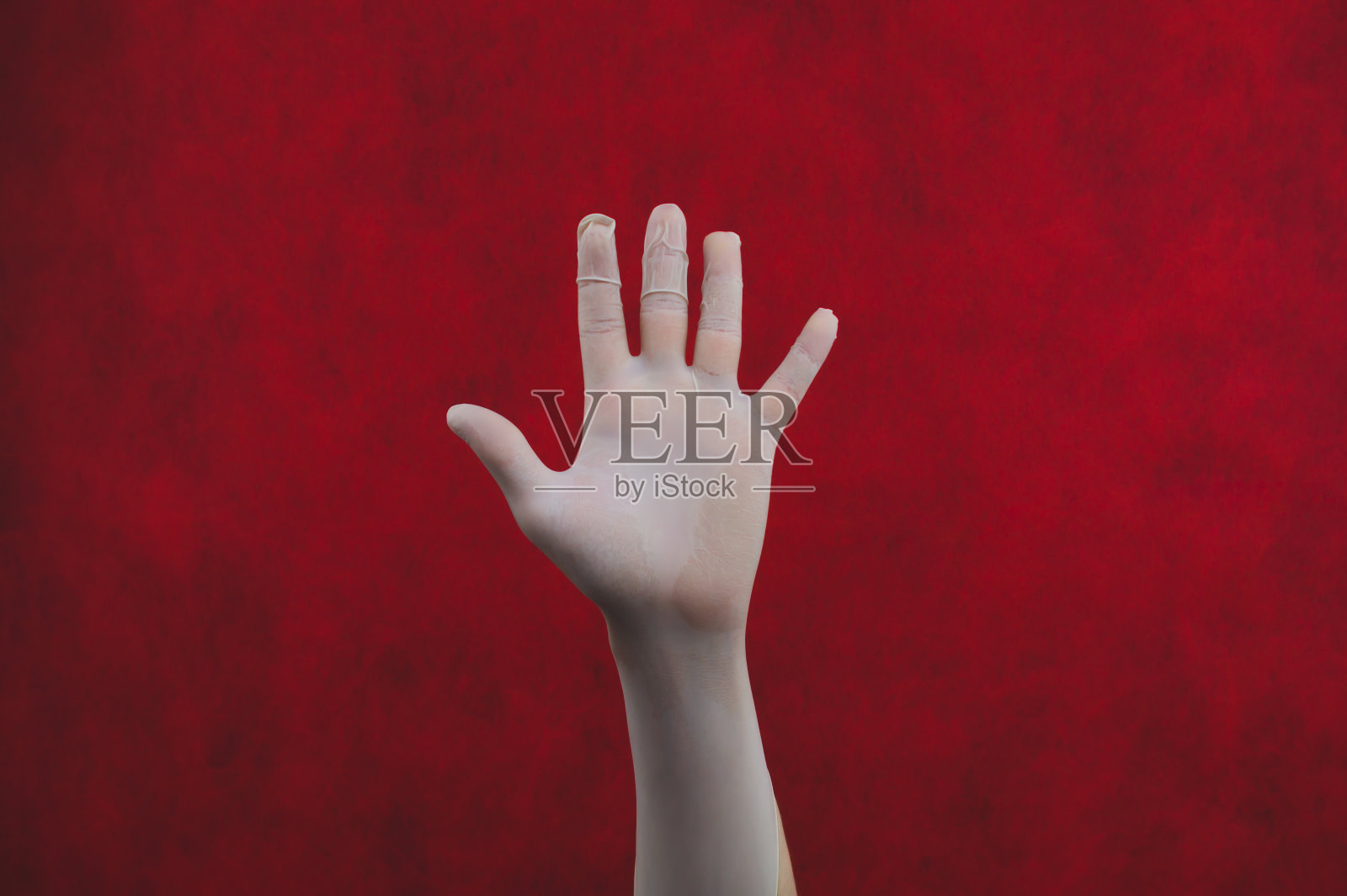 红色背景上戴着医用手套的手掌。戴着白色防护手套的手照片摄影图片