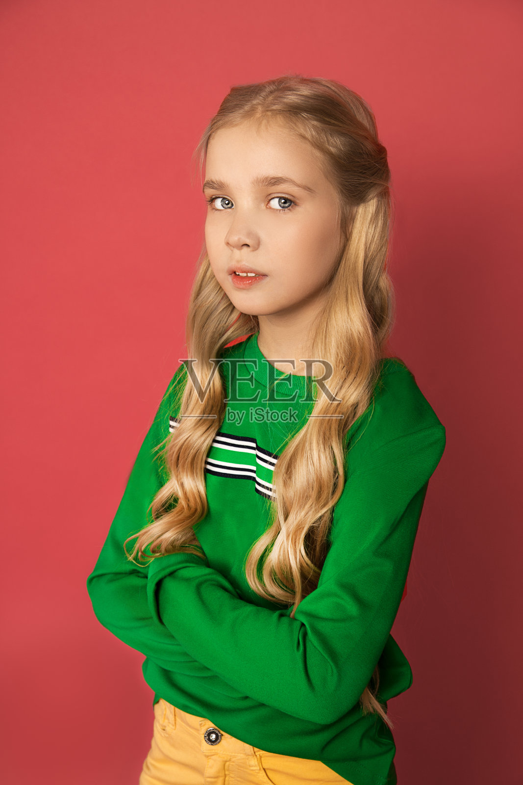 一个美丽甜美严肃的女孩，8-10岁，金发，蓝色或灰色的眼睛，卷曲的头发，鲜艳的衣服在粉红色的背景。紧急照片在工作室。特写肖像。照片摄影图片