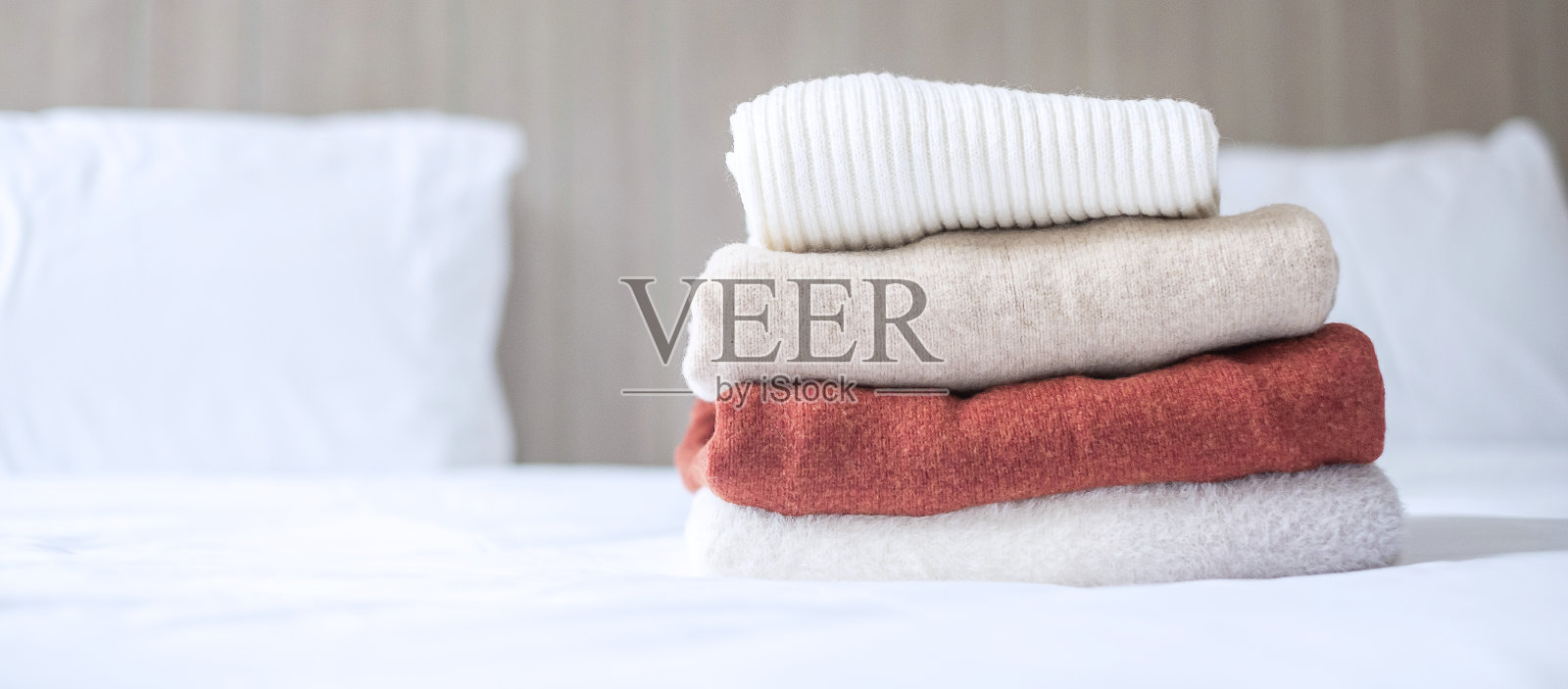 在豪华酒店、度假村或家中的床上堆放米色羊毛衫。放松，秋冬衣服，洗衣和度假概念照片摄影图片