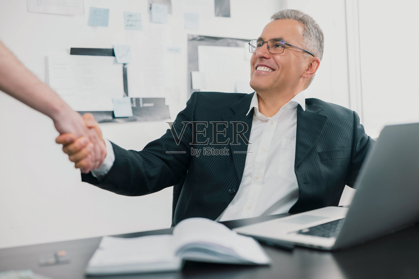 英俊的白发商人优雅的西装坐在现代明亮的办公室与商业伙伴握手后的成功谈判，合作的工作理念照片摄影图片