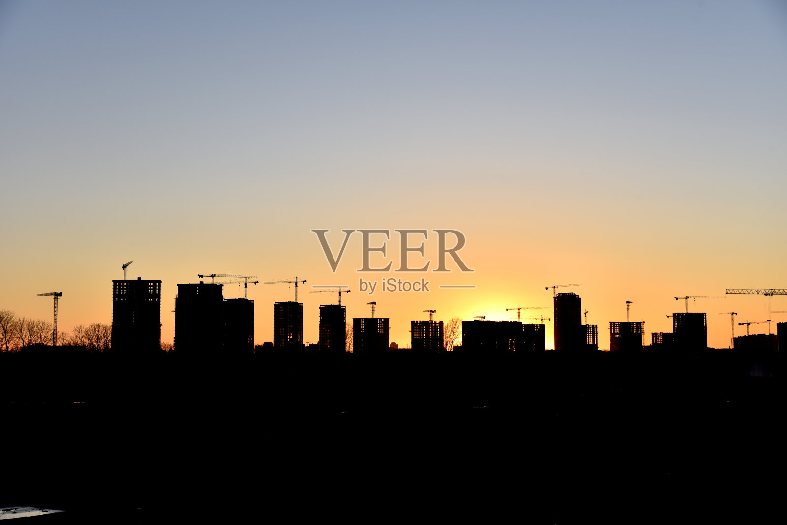 塔吊和建筑者的剪影在日落的背景上行动。工人在模板和浇筑混凝土期间，通过混凝土泵车连接到预拌卡车。混凝土泵送照片摄影图片