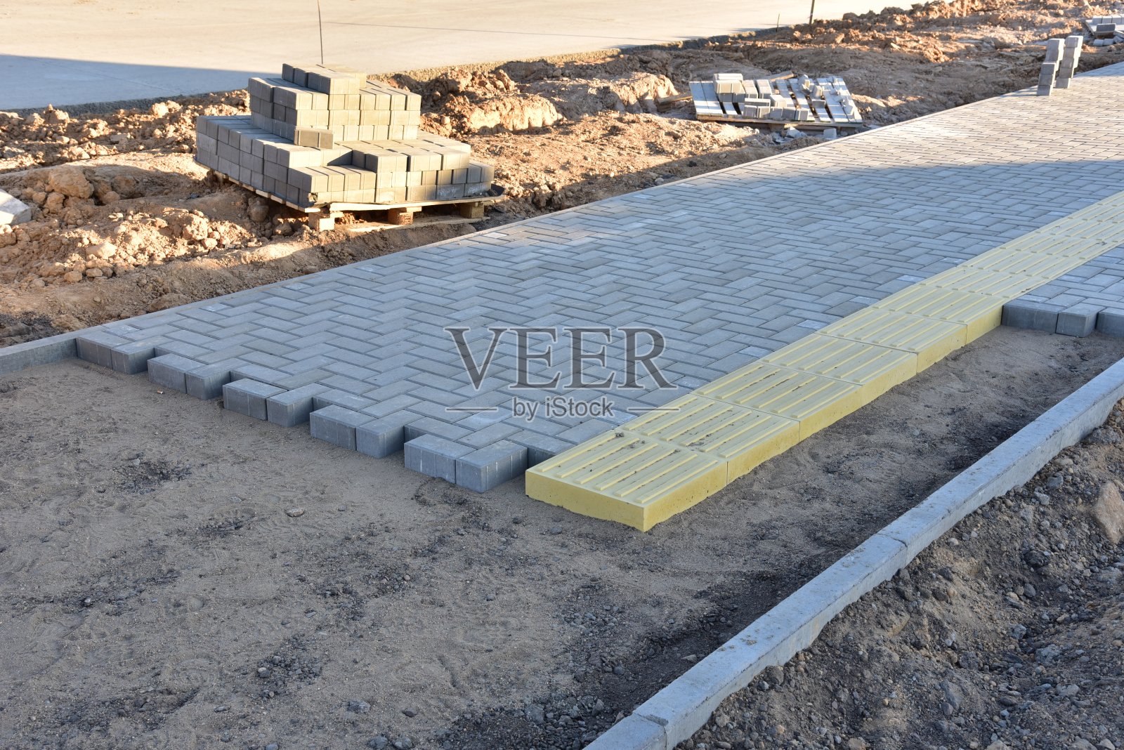 在建筑地盘铺设铺路板。在城镇步行区安装铺路砖的过程。铺砌混凝土砌块用的砂。路面翻新工程照片摄影图片