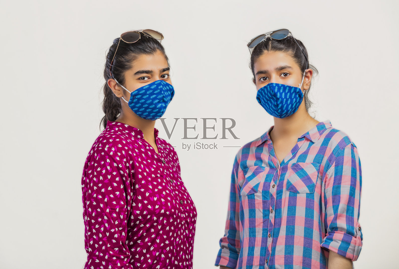 两个快乐的女孩站在太阳眼镜的脸上，戴着面罩，看着镜头照片摄影图片